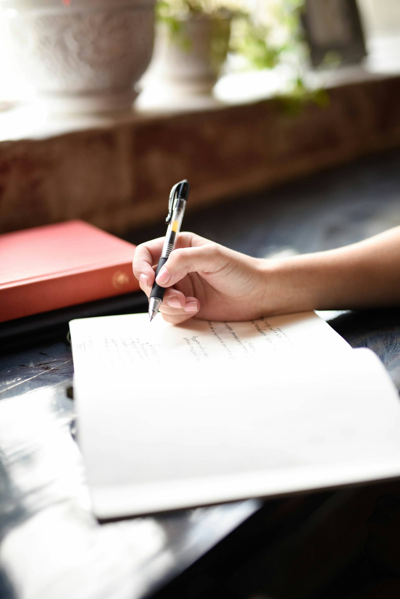 Hands writing in pen on an open notebook.